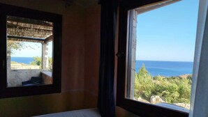 A bedroom with a bed, a window with a view of the sea, and a small balcony.