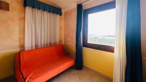 A room with a single orange sofa, a window with blue curtains, and a view of a cityscape.