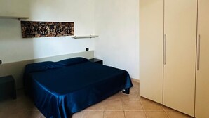 A bedroom with a bed, a wardrobe, and a wall-mounted shelf with artwork.