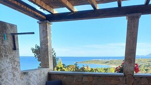A covered outdoor seating area with a view of the sea and landscape.