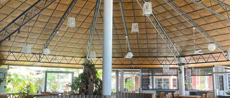 Un espacio interior amplio con techo alto y una columna central, rodeado de mesas y sillas de madera.
