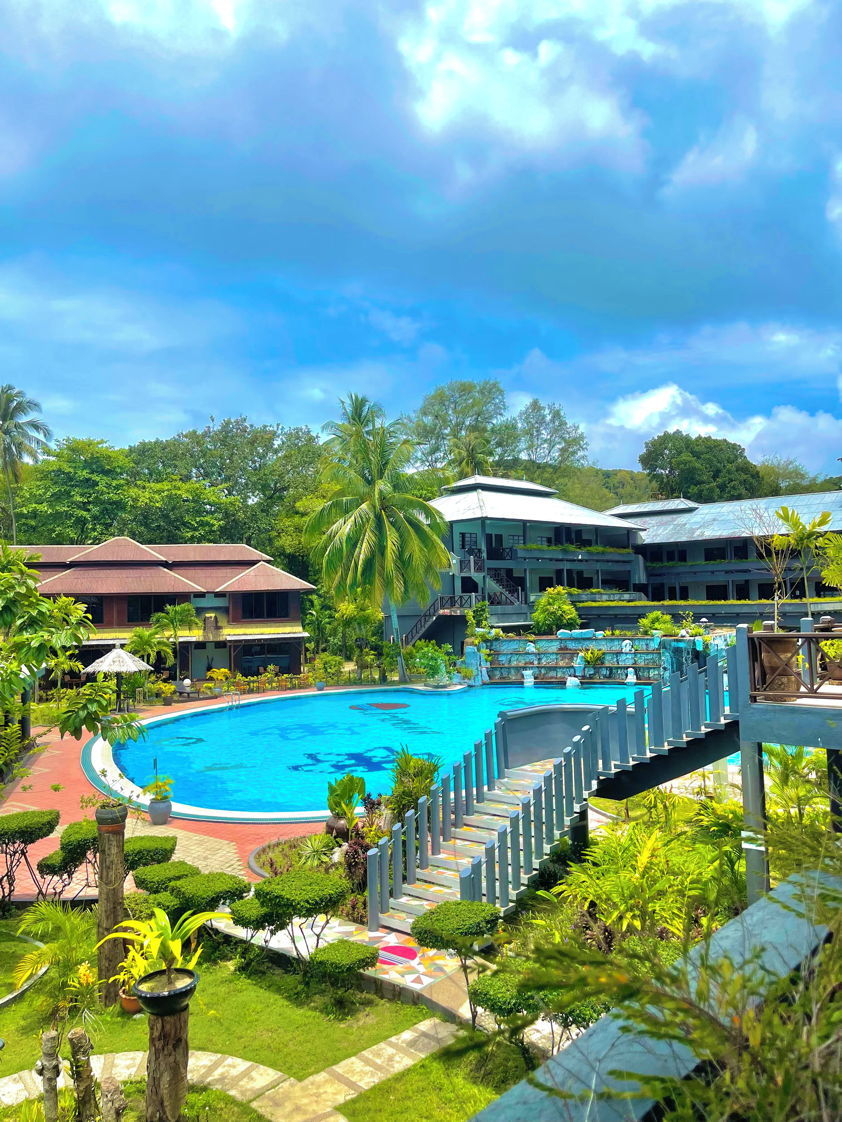 A resort with a swimming pool, palm trees, and a multi-story building.