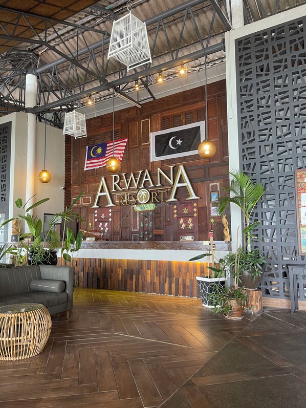 A reception area with a wooden reception desk, a flag of Malaysia, and a sign reading 'ARWANA RESORT'.