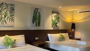 A hotel room with two beds, each with white linens and green leaf-patterned pillows. There are wall-mounted air conditioning units and a bedside table with a lamp. - Arwana Beach Resort - Perhentian (Pulau Perhentian Besar)