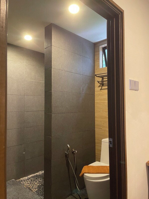 Un baño moderno con paredes de baldosas oscuras, zona de ducha y un inodoro.