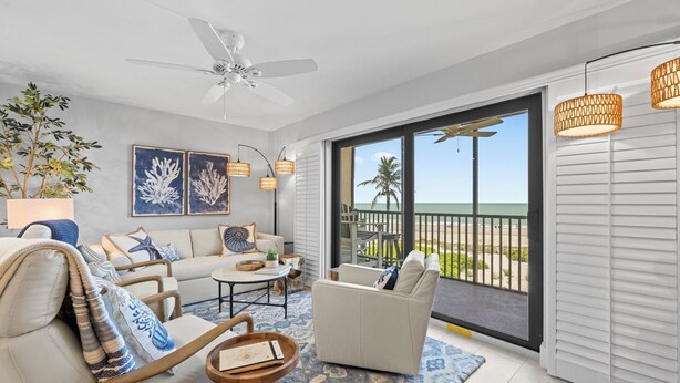 A spacious living room with a large window overlooking the beach, a ceiling fan, and a cozy seating area with a coffee table. - OCEAN'S REACH 3X3: 1-Bdrm, 3rd Floor, Gulf Front Views, All Amenities Open! (Sanibel Island)