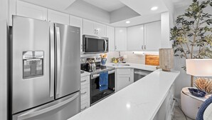 A modern kitchen with stainless steel appliances, white cabinetry, and a marble countertop. - OCEAN'S REACH 3X3: 1-Bdrm, 3rd Floor, Gulf Front Views, All Amenities Open! (Sanibel Island)