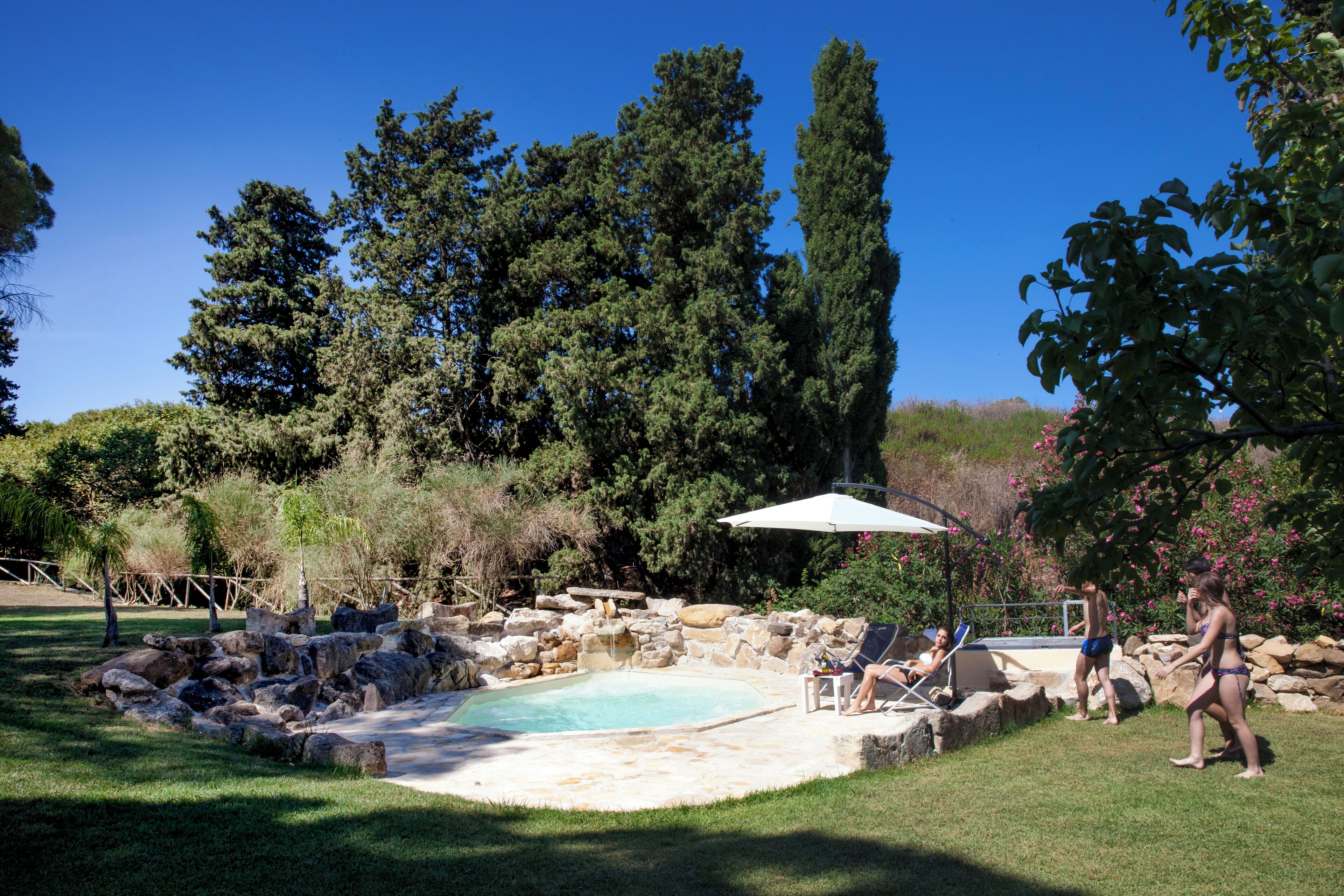 Un jardin à l’arrière de la maison avec une piscine, entouré de rochers et d’arbres.