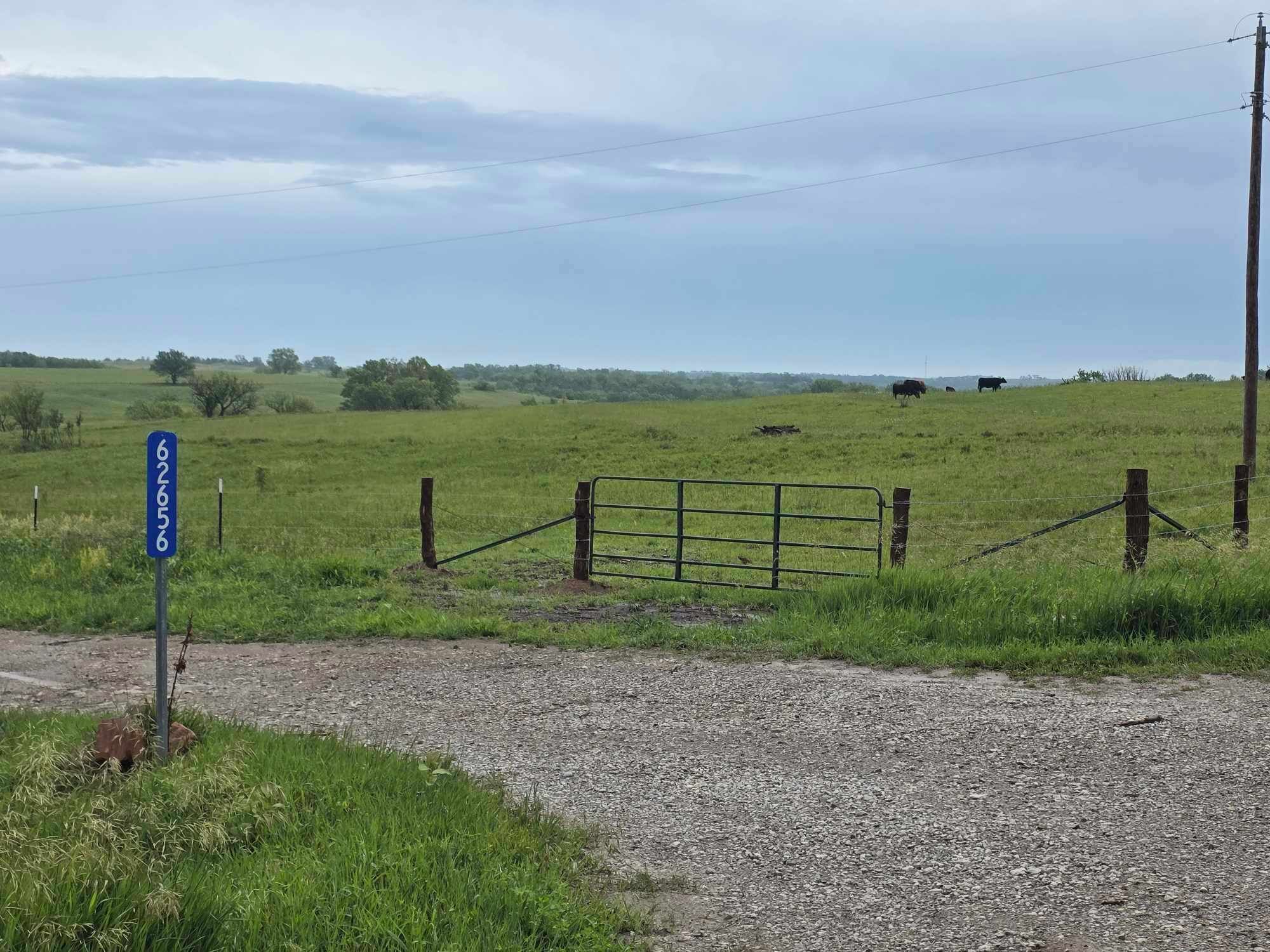 A rural landscape with a gravel path, a metal gate, and a blue sign with numbers.