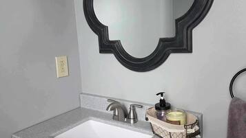 Ein Badezimmer mit einem weißen Waschbecken, einem modernen Wasserhahn, einem schwarzen Spiegelrahmen und einem Handtuchhalter.