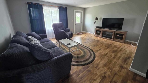 Una sala de estar con un sofá, sillones, una mesa de centro, un televisor y piso de madera.