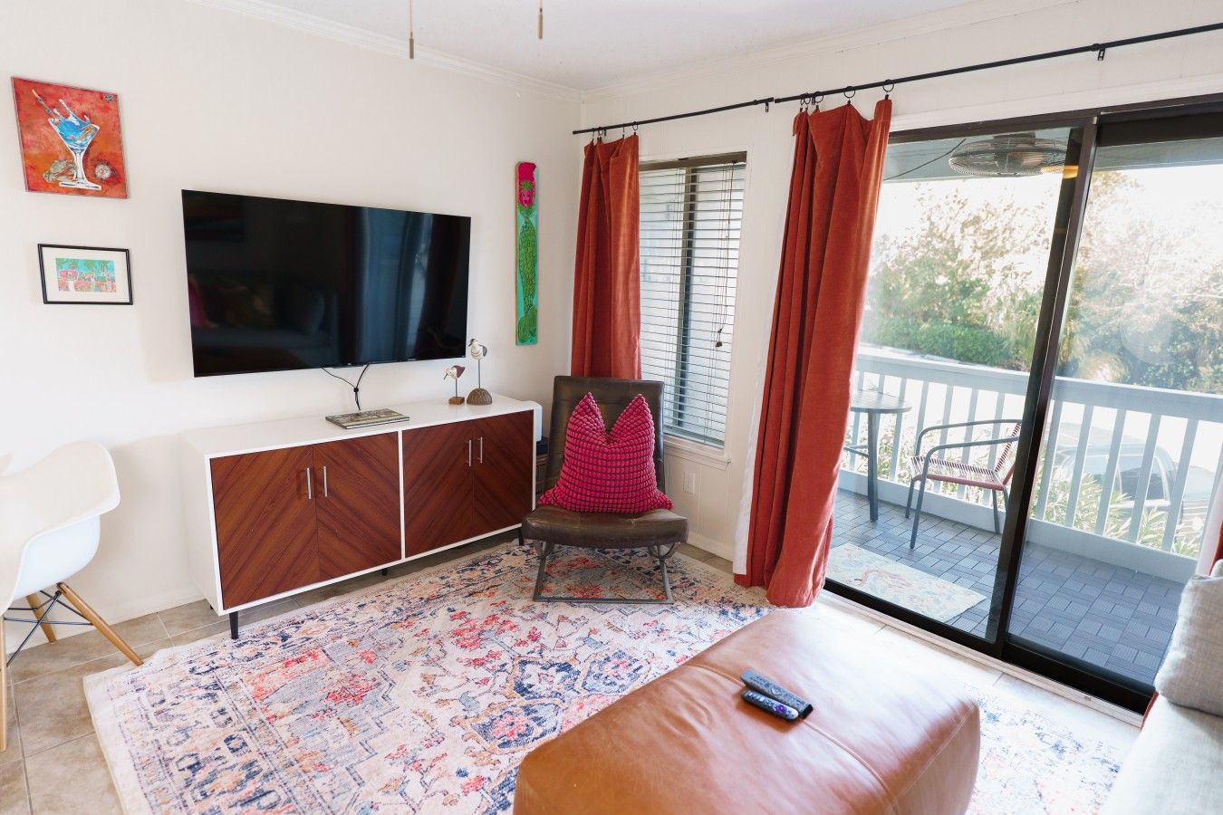 Un salon doté d’un téléviseur à écran plat, d’un canapé en cuir marron, d’un tapis à motifs, d’une chaise blanche et d’un balcon avec vue.