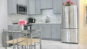 A modern kitchen with grey cabinets, a stainless steel refrigerator, a microwave, and a dining table with chairs.