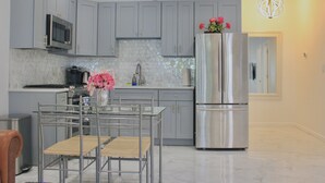 A modern kitchen with grey cabinets, stainless steel appliances, and a dining area with a glass table and chairs.