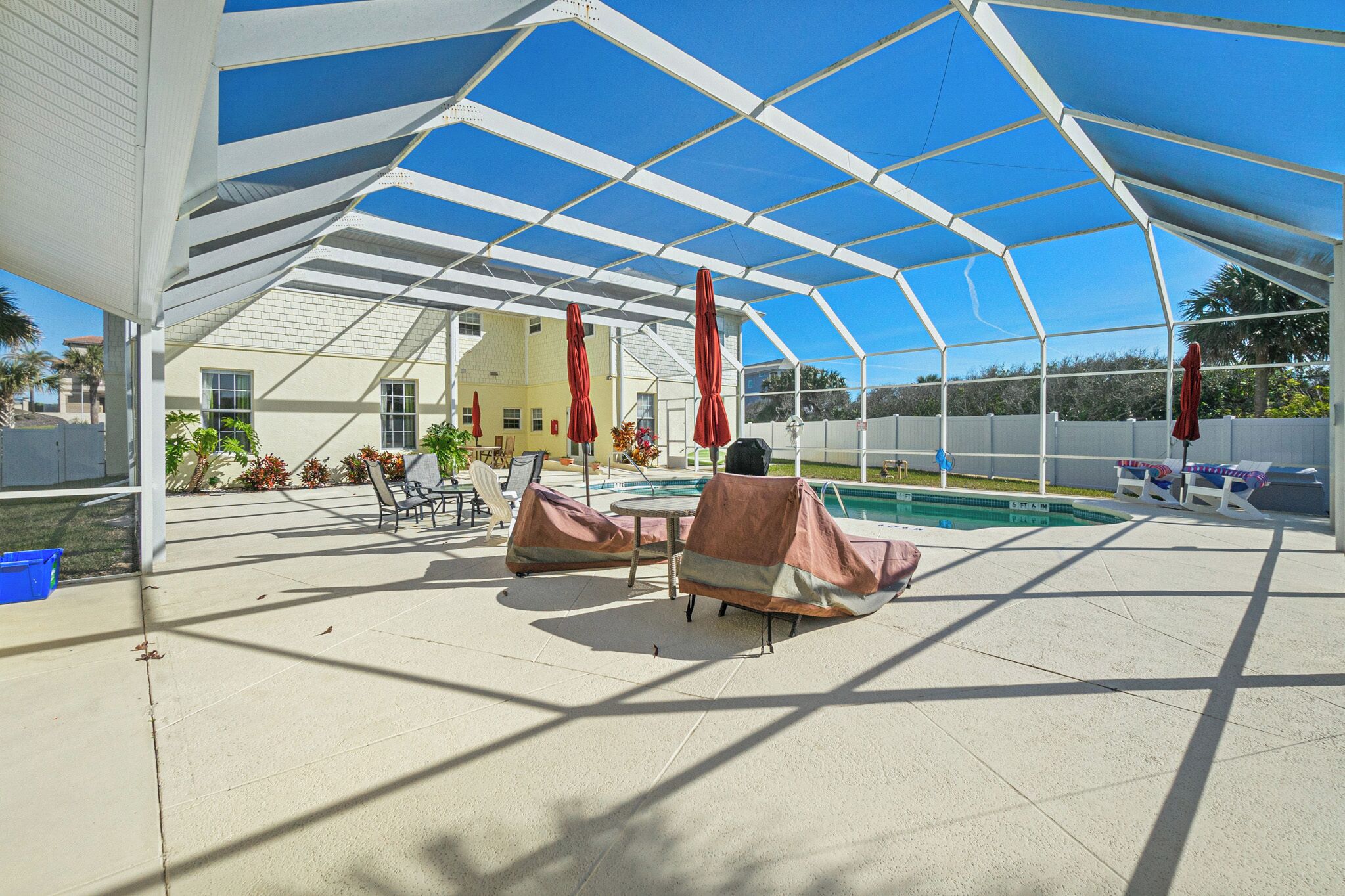 Un espacio al aire libre techado con piscina, sillas de descanso y sombrillas.