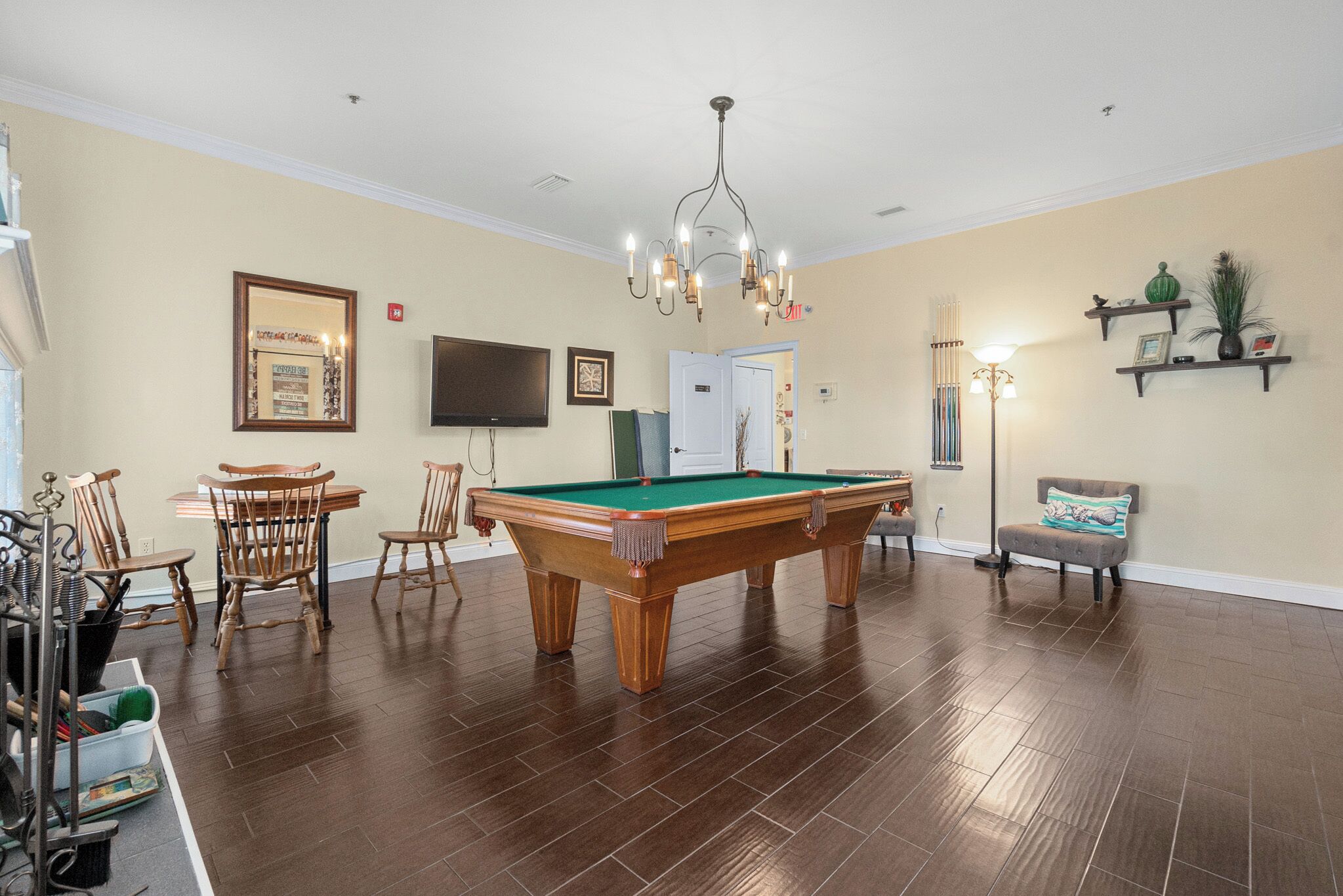 A room with a pool table, wooden chairs, a television, and a chandelier.