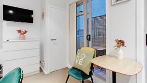 Une chambre moderne équipée d’un téléviseur à écran plat, d’une table à manger, d’une chaise agrémentée d’un coussin orné du mot « LOVE », et d’une petite table sur laquelle est posé un vase de fleurs.