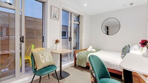 Une chambre moderne avec un lit, une petite table, une chaise et un balcon équipé de stores en bois.