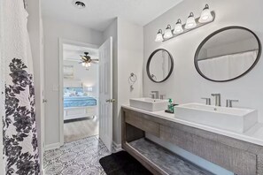 Ein modernes Badezimmer mit zwei Waschbecken, einem großen Spiegel und einem Deckenventilator.