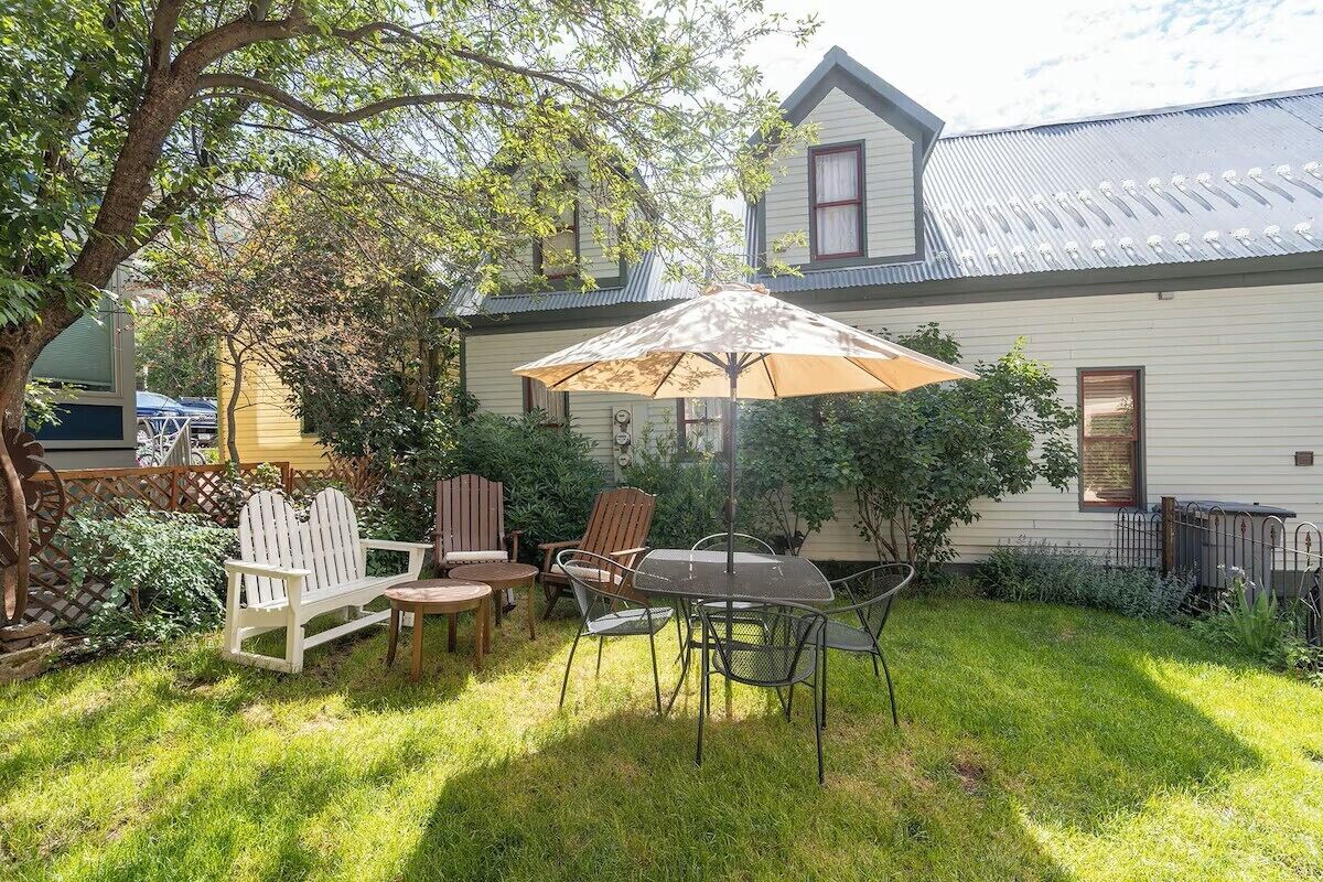 A backyard with a dining table, chairs, and an umbrella.