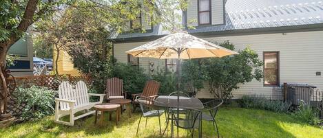 A backyard with a dining table, chairs, and an umbrella.