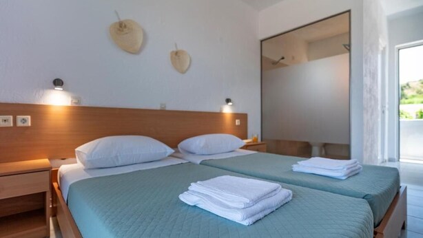 Habitació d'hotel amb dos llits, un panell de fusta al capçal, una tauleta de nit i un mirall gran.