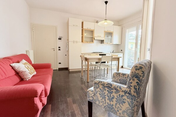 A compact living space with a kitchenette, a red sofa, a patterned armchair, and a door leading to an outdoor area.