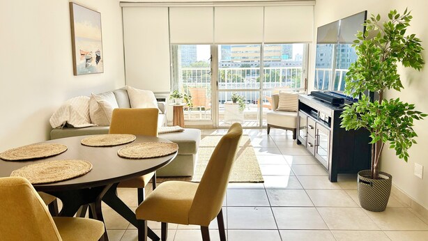 Una sala de estar moderna con comedor, sofá, televisor y balcón con vista a la ciudad.