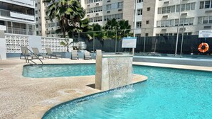 Una piscina con cascada, rodeada de sillas de descanso y una palmera.