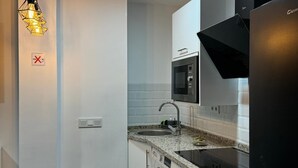 A modern kitchen with white cabinets, a black refrigerator, a built-in oven, and a washing machine. - LINERLIFE APARTMENT (Málaga)