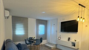 A modern living room with a blue sofa, a dining area with a table and chairs, a mounted TV, and a built-in bench with storage. - LINERLIFE APARTMENT (Málaga)