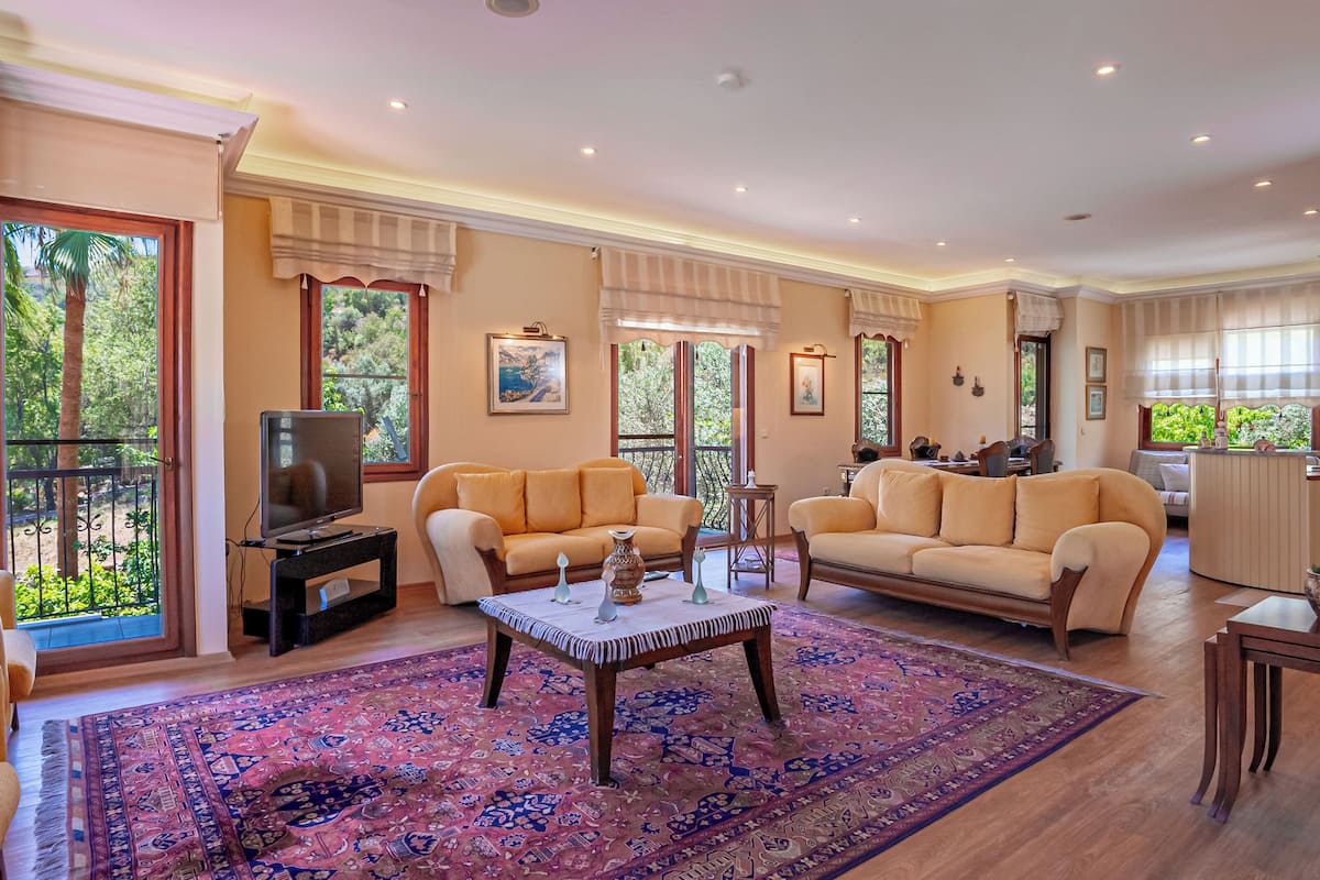 A spacious living room with a large rug, sofas, a coffee table, and a television.