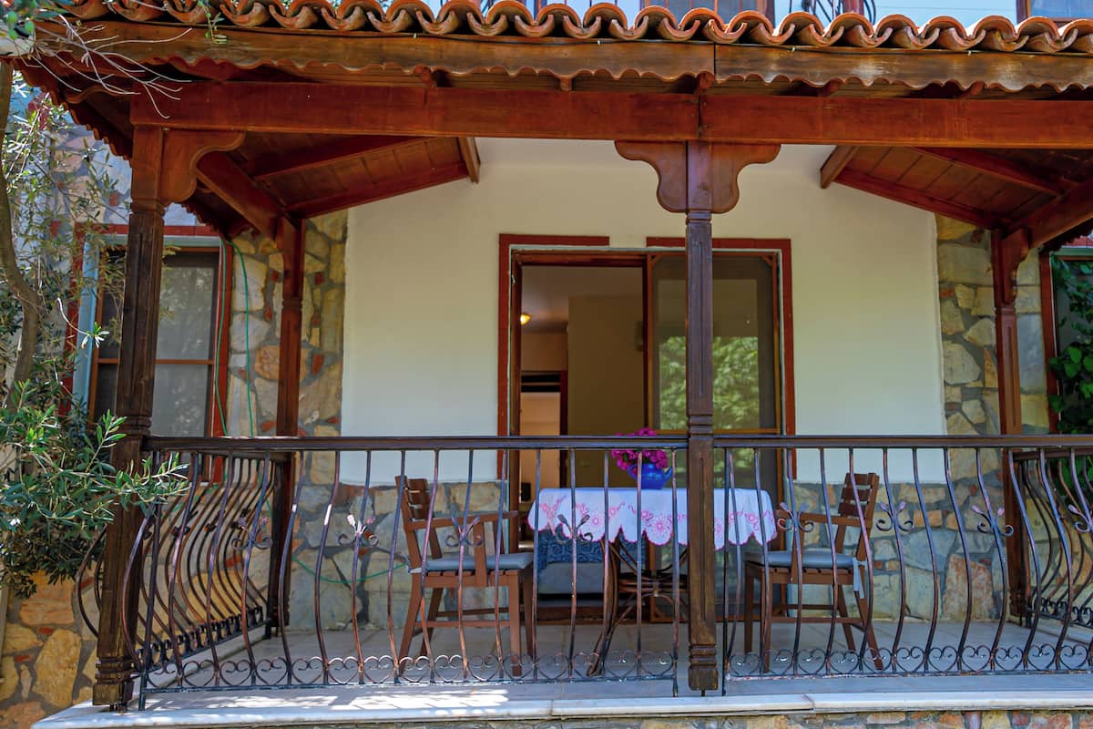 A wooden porch with a tiled roof, a table with a tablecloth, and chairs.