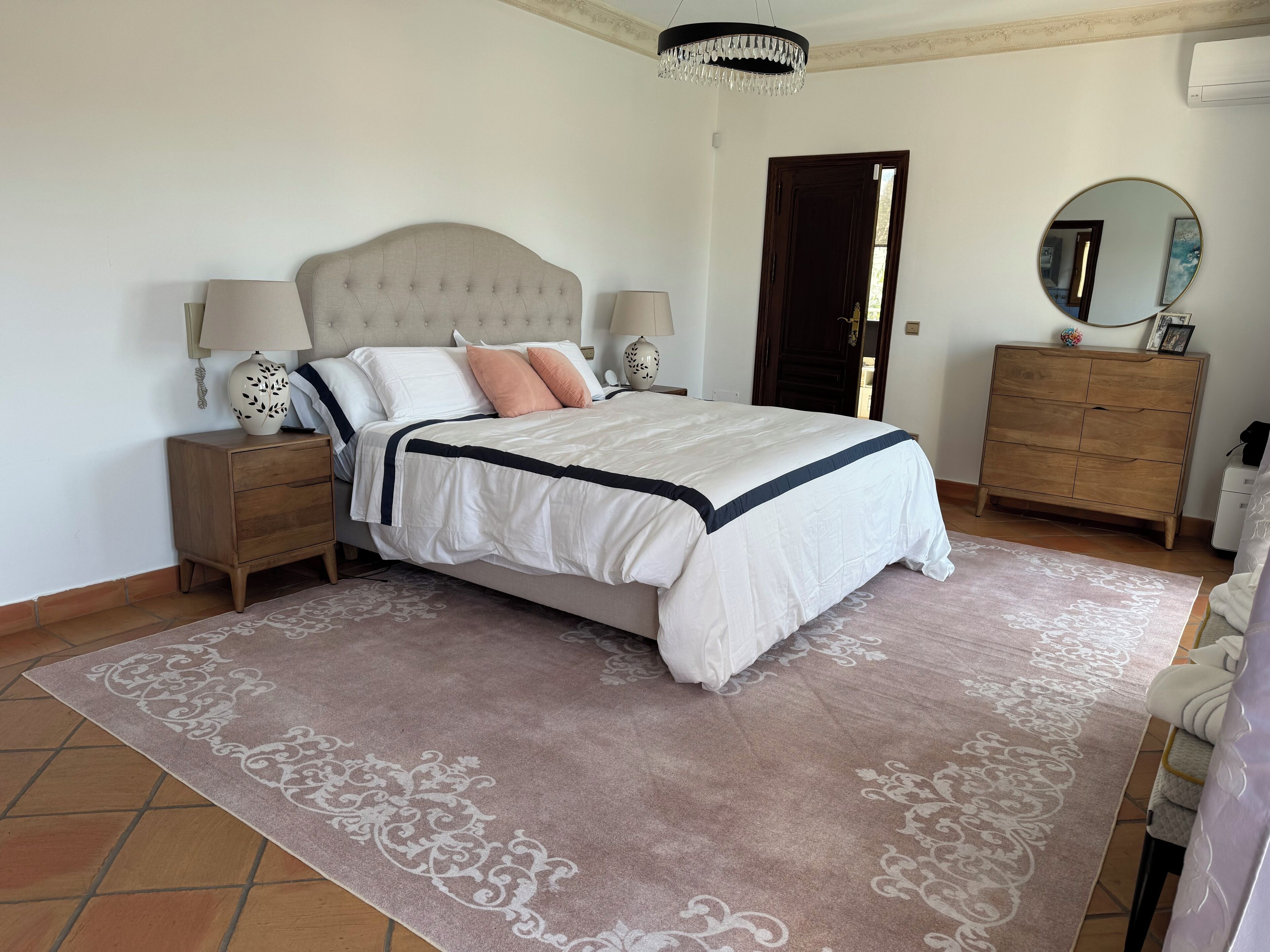 A bedroom with a bed, nightstands, a dresser, a chandelier, and a mirror.