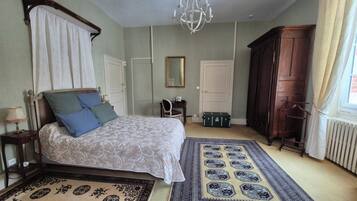 A bedroom with a four-poster bed, a chandelier, a wooden wardrobe, and two rugs.
