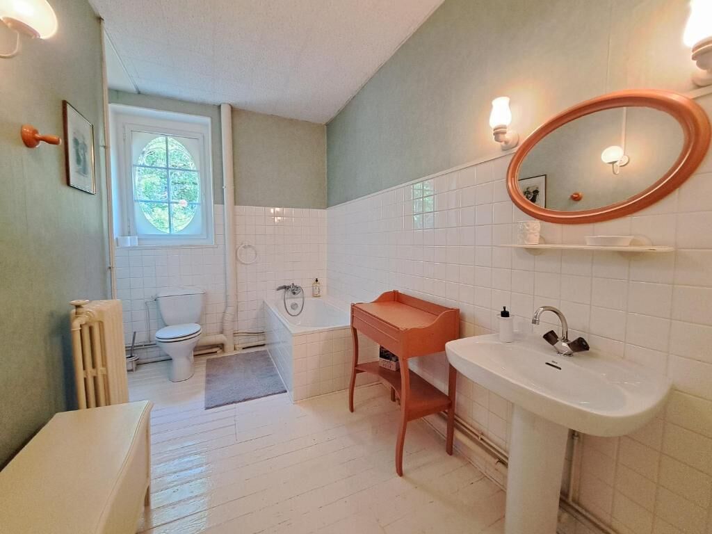 Un bagno con un lavandino bianco, un mobile bagno in legno, uno specchio rotondo e una vasca da bagno.