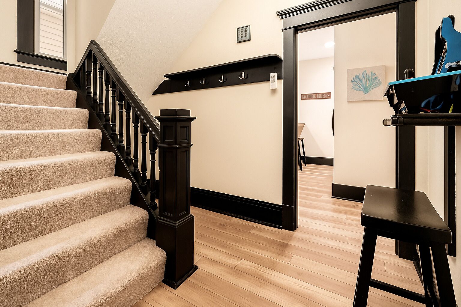 A staircase with a dark wooden handrail and beige carpeted steps leading to a room with a wooden floor.