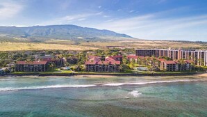 Un hotel sulla costa con diversi edifici, spiaggia privata e montagne sullo sfondo.