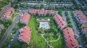 A hotel with multiple red-roofed buildings, a central swimming pool, and surrounding greenery. - South Kihei resort 1 bedroom condo, AC, across street from beach, walkable area (Wailea-Makena)