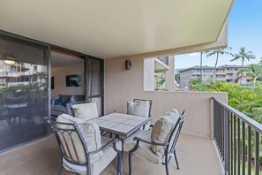 A balcony with a table and chairs, a sliding glass door, and a view of palm trees and buildings. - South Kihei resort 1 bedroom condo, AC, across street from beach, walkable area (Wailea-Makena)