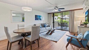 Ein modernes Wohnzimmer mit Esstisch, Stühlen, einer Couch, einem Couchtisch, einem Deckenventilator und Blick ins Freie durch eine Glastür.
