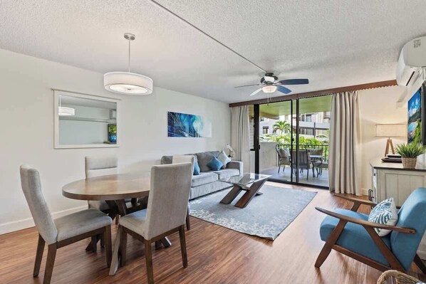 A modern living room with a dining table, chairs, a sofa, a coffee table, a ceiling fan, and a view through the glass door to the outside. - South Kihei resort 1 bedroom condo, AC, across street from beach, walkable area (Wailea-Makena)