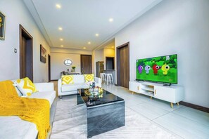 A modern living room with a large flat-screen TV, a sofa, a coffee table, and a kitchen area in the background. - 2 Bedroom at Skynest Residency Westlands (Nairobi)