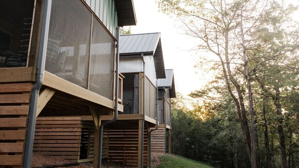 Un bâtiment moderne doté de grandes fenêtres et d’un toit en pente, entouré d’arbres.