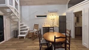 Une cuisine compacte dotée d’un îlot central, d’un coin repas avec une table ronde et des chaises, et d’un escalier avec une étagère intégrée.