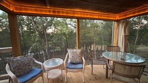 Un espace extérieur aménagé, abrité et doté de chaises en osier et d’une table en verre, offrant une vue sur une zone boisée.