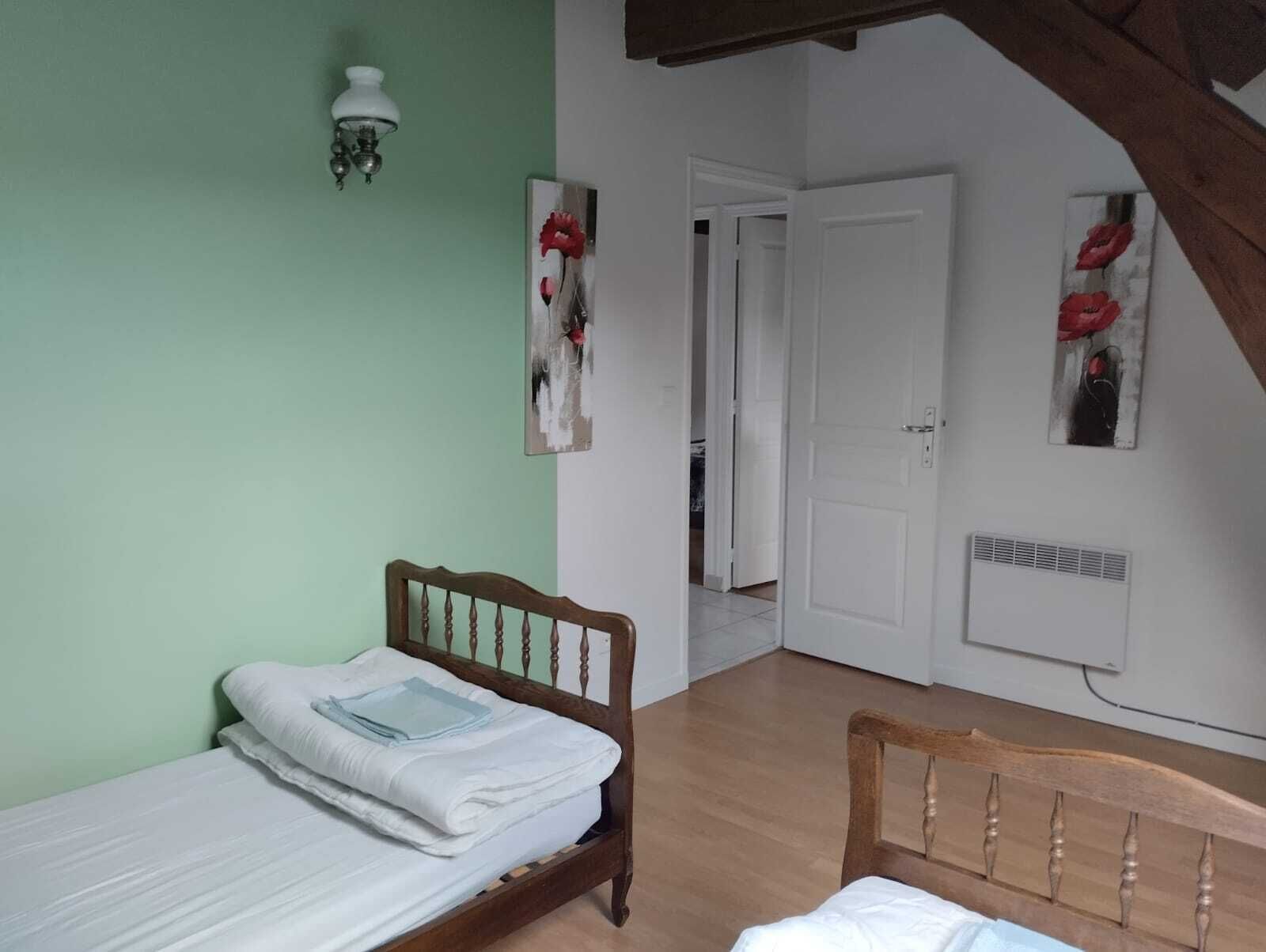 A bedroom with a bed, a nightstand, a wall-mounted lamp, and a door leading to another room.