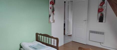 A bedroom with a bed, a nightstand, a wall-mounted lamp, and a door leading to another room.