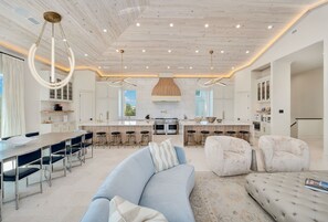 Eine geräumige Küche mit einer zentralen Kochinsel, Barhocker und einem Essbereich mit einem hellblauen Sofa.