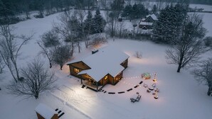 A snow-covered landscape with a wooden cabin featuring a porch and outdoor seating area.